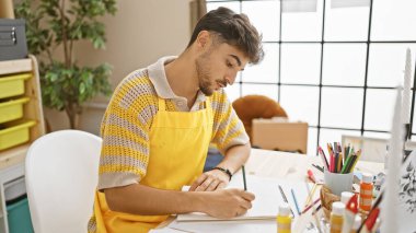 Yakışıklı genç bir Arap, kendini adamış bir sanatçı, canlı bir sanat stüdyosunda defterine kendini tamamen kaptırmış.