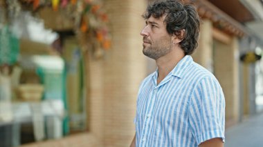 Latin kökenli genç adam ciddi bir ifadeyle sokağa bakıyor.