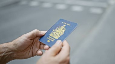 Gri saçlı orta yaşlı bir adam, sıradan bir şekilde, güneşli, kentsel bir sokakta vatansever bir şekilde dururken, Kanada pasaportunu ortaya çıkarıyor..