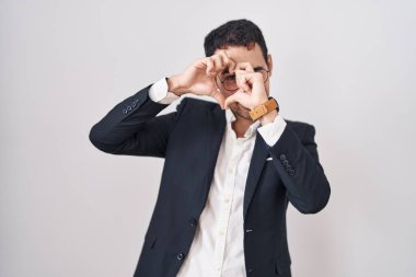 Yakışıklı İspanyol bir adam beyaz arka planda duruyor. El ve parmaklarıyla kalp şekli yapıyor. İşaretten bakıp gülümsüyor. 