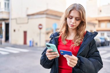 Sokakta akıllı telefon ve kredi kartı kullanan genç sarışın kadın.