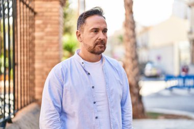 Sokakta ciddi bir ifadeyle yan tarafa bakan beyaz bir genç.