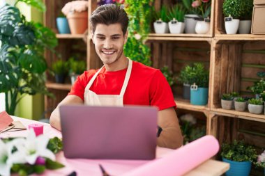 Young hispanic man florist smiling confident using laptop at flower shop