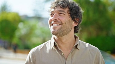 Genç İspanyol adam gülümsüyor parkın kenarına bakıyor.