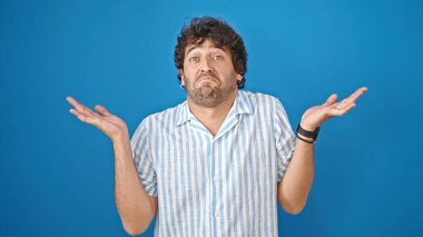 İzole edilmiş mavi arka planda hiçbir şeyden habersiz duran İspanyol genç adam.