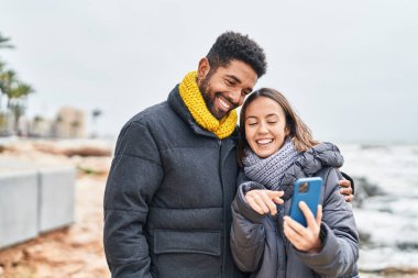 Man and woman couple smiling confident using smartphone at seaside