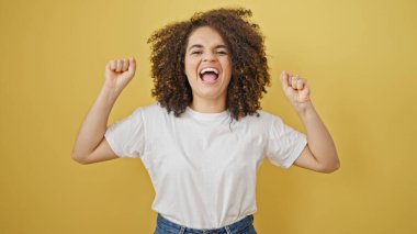 Genç, güzel, İspanyol bir kadın gülümsüyor. Kazanan kişinin sarı arka planda yaptığı jestle duruyor.