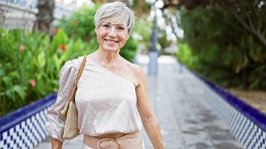 Yeşillik ve seramik döşemeleri olan bir bahçede gülümseyen olgun İspanyol kadın..