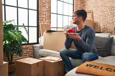 Genç İspanyol adam yeni evindeki kanepede kahve içiyor.