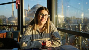 Genç bir kadın İstanbul 'da arka planda hagia sogası olan bir restoranda çay içiyor, hindi..