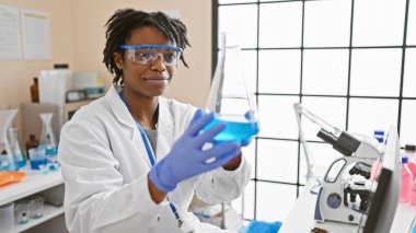 Modern laboratuvar ortamında bir matarayı inceleyen Afrikalı kadın bilim adamı.