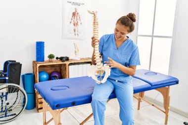Güzel İspanyol kadın fizyoterapist gülümsüyor. Rehabilitasyon kliniğinde omurganın anatomik modelini tutuyor.