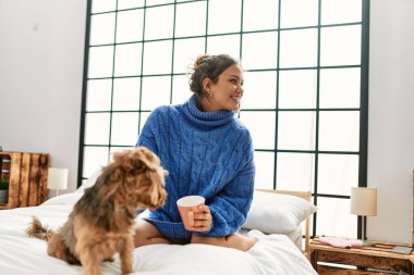 Genç, güzel, İspanyol bir kadın. Bir fincan kahve içiyor. Yatakta köpekle oturuyor.