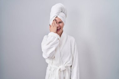 Sarışın, beyaz kadın bornoz giyiyor. Bir gözünü eliyle kapatıyor. Yüzünde kendine güvenen bir gülümseme ve şaşırtıcı bir duygu var.. 