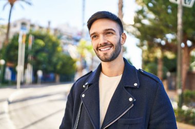 Young hispanic man smiling confident looking to the side at street