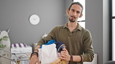 Çamaşır odasında elinde sepet tutan İspanyol genç adam.