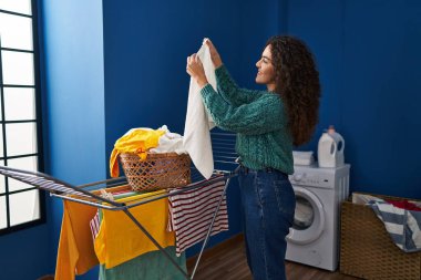 Genç ve güzel İspanyol kadın gülümsüyor çamaşırhanede çamaşır ipine asılan kendine güvenen kıyafetler.
