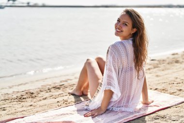 Genç ve güzel İspanyol kadın turist kumsalda otururken gülümsüyor.