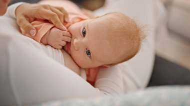 Anne ve kız kanepede oturup bebeği emziriyorlar.