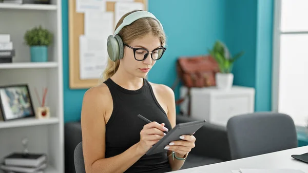 Young blonde woman business worker writing on touchpad listening to music at the office