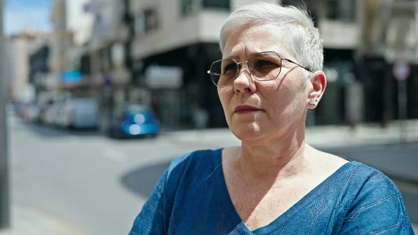 Middle age grey-haired woman looking to the side with serious expression at street