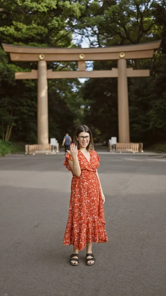 Beautiful brunette adult woman, a confident latin of hispanic origin, at tokyo\'s meiji shrine, spots me, invitingly waves hello using a friendly and positive gesture, requesting my company