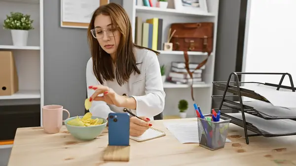 Brunette Woman Multitasks Modern Office Writing Notes While Snacking Checking — Stock Photo, Image
