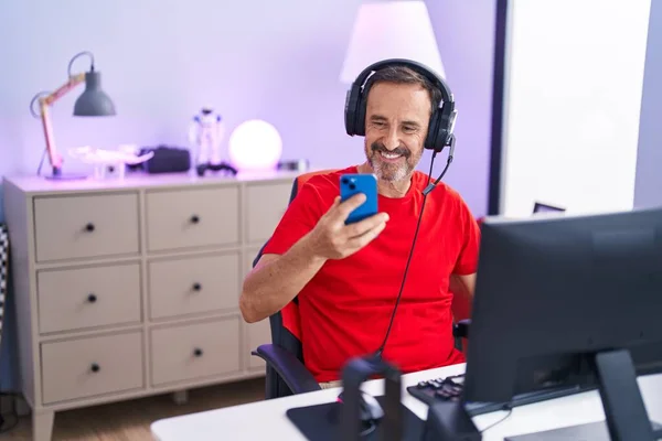 Middle age man streamer using computer and smartphone at gaming room