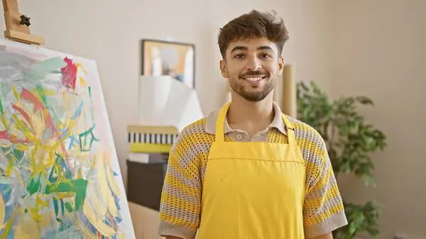 Handsome young arab man, a confident artist with a warming smile, standing proudly in his art studio