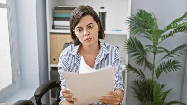 Young beautiful hispanic woman business worker reading document at the office
