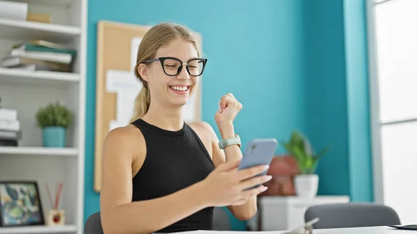 Young blonde woman business worker using smartphone with winner gesture at the office