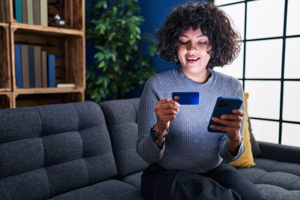 年轻美丽的惊慌失措的女人坐在家里沙发上 用智能手机和信用卡 — 图库照片