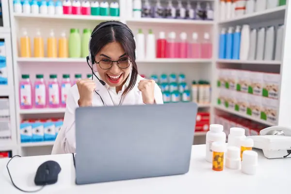 Young arab woman working at pharmacy drugstore using laptop celebrating surprised and amazed for success with arms raised and open eyes. winner concept.