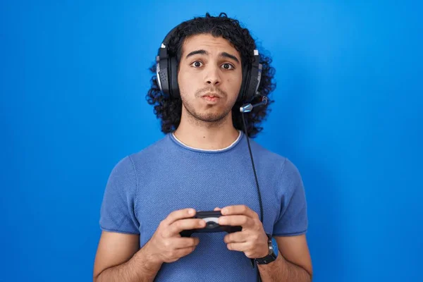 一个西班牙裔男人 卷发玩电子游戏 手握控制器 用滑稽的脸蛋鼓起双颊 嘴被空气吹胀 — 图库照片