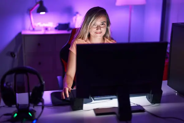 Young blonde woman streamer playing video game using computer at gaming room