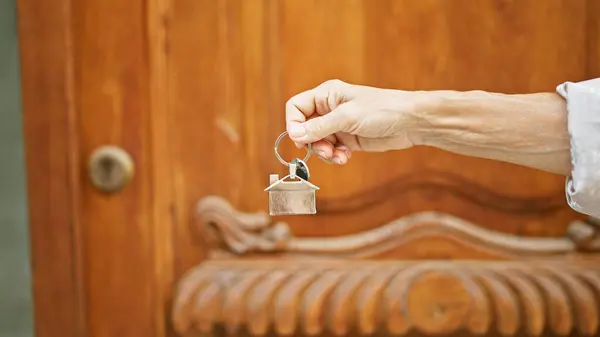 Mature Woman Hand Holding House Keys Front Wooden Door Signifying — Stock Photo, Image