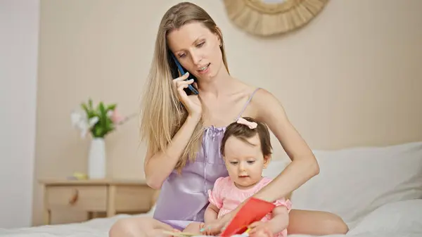 Mother and daughter talking on smartphone reading book on bed at bedroom