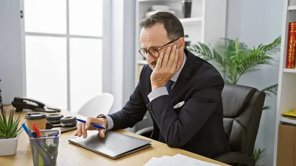 Worried middle age man with grey hair at work, a worried, grey-haired businessman sitting at his office desk, wrestling with doubts.