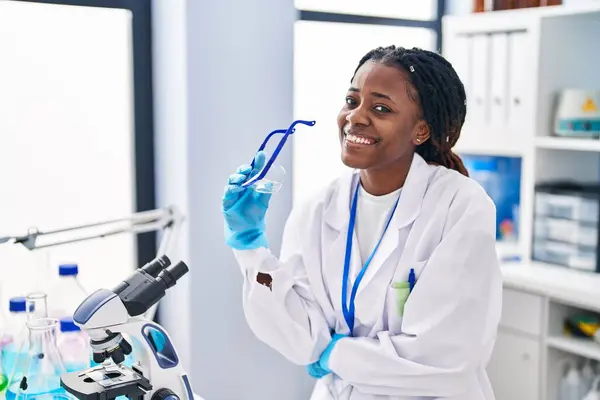 African american woman scientist smiling confident holding security glasses at laboratory