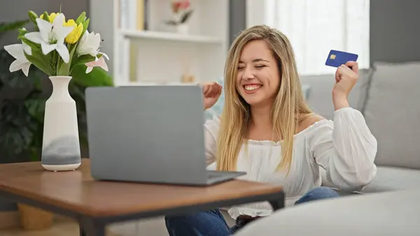 Young blonde woman shopping with laptop and credit card sitting on floor at home
