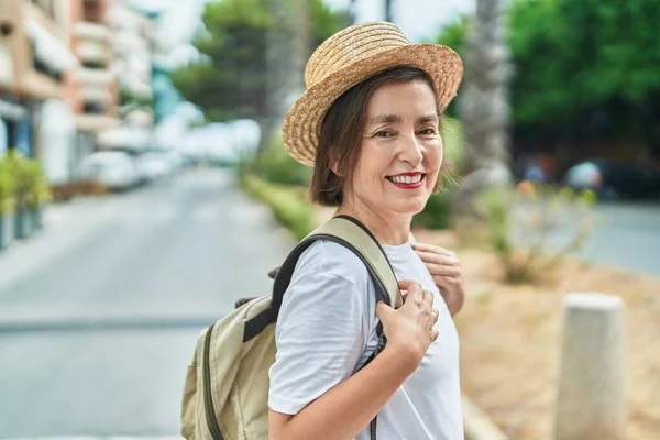 Middle age woman tourist smiling confident wearing backpack at street