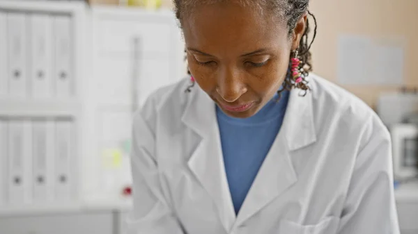 African american woman in white lab coat focused on work in a medical laboratory setting.