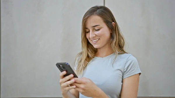 陽気な街のストリートでデジタル会話に従事して彼女のスマートフォンに幸せに触れる陽気な若いブロンドの女性 — ストック写真