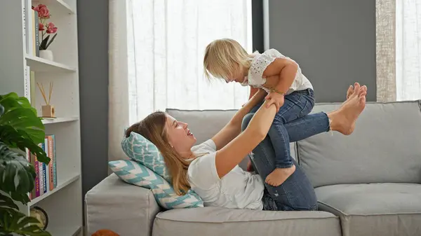Confident caucasian mother and daughter lying comfortably on a sofa, playing and smiling in the warmth of their home