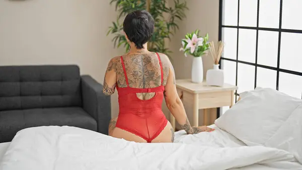 Hispanic woman with amputee arm wearing lingerie sitting on bed backwards at bedroom