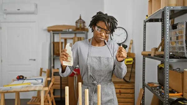 A woman in a workshop holding money with a confused expression, surrounded by tools and wooden materials.