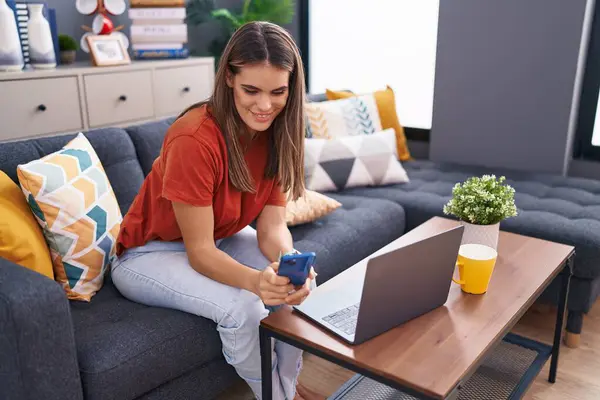 Young Beautiful Hispanic Woman Using Smartphone Laptop Sitting Sofa Home — Stockfoto