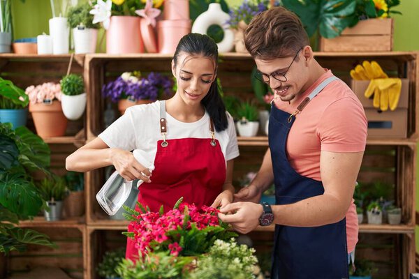 Man and woman florists using diffuser watering plant at flower shop