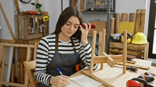 一位心事重重的女士在一间有工具环绕的木工工作室里勾画出了一些家具的草图 — 图库照片