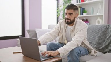 Modern bir oturma odasında dizüstü bilgisayar kullanan sakallı genç bir adam..